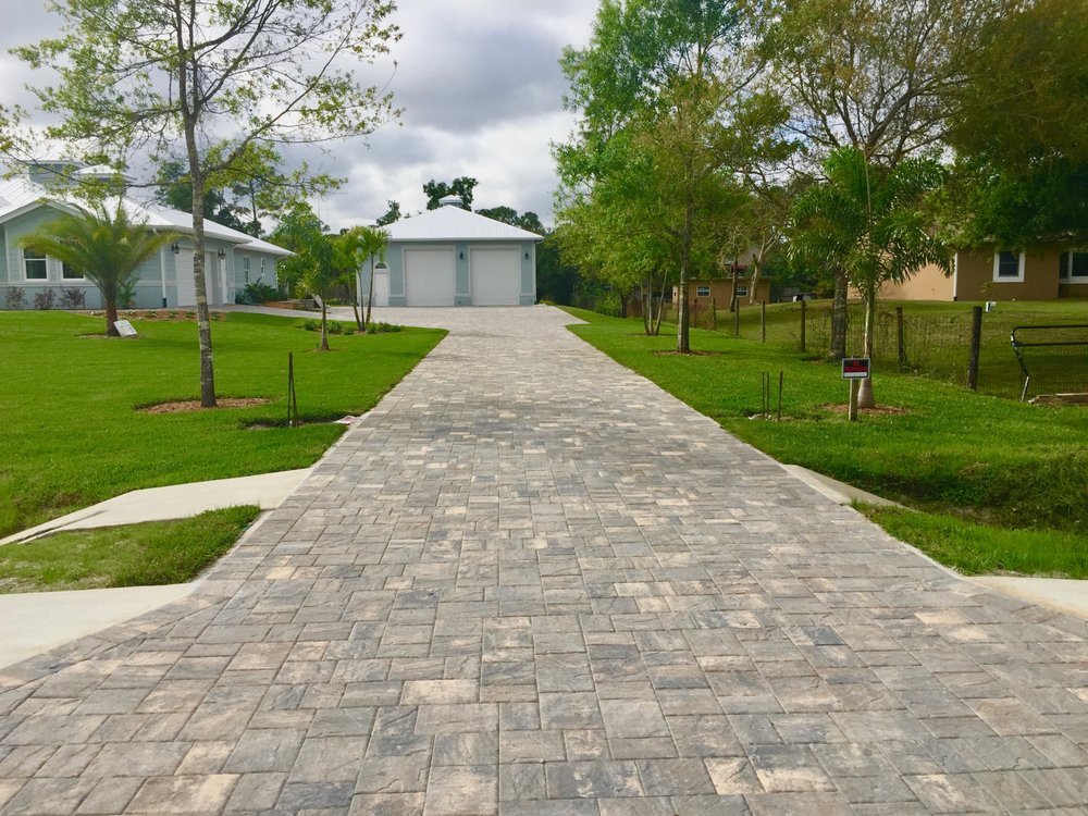 Long gray paver driveway leading to a residential garage