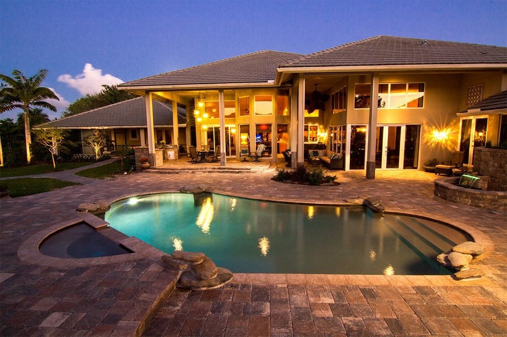 Paver pool deck and illuminated Florida home at dusk