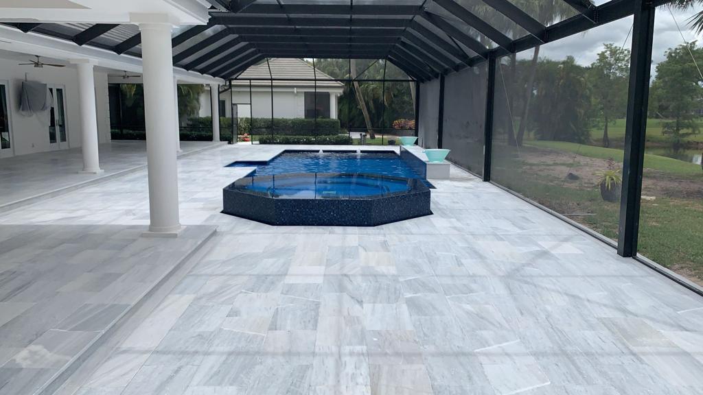 Screened swimming pool and raised spa surrounded by pale stone pavers